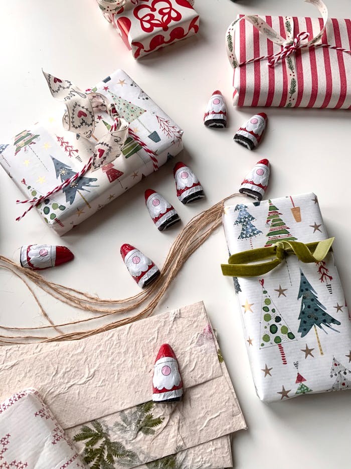 Christmas gifts wrapped in colorful paper with mini Santa decorations on a white surface.