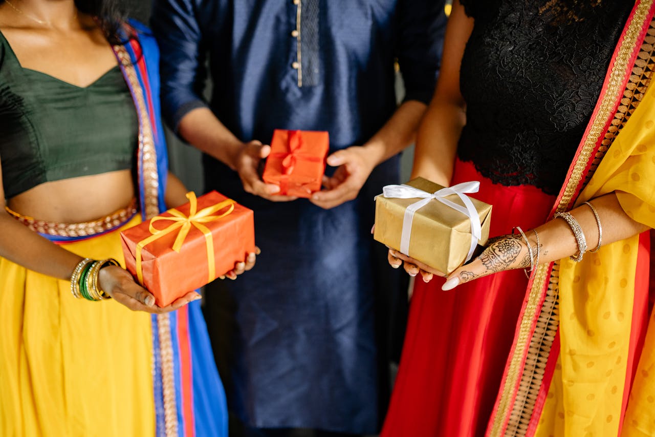 People in traditional Indian clothing exchanging gifts during a festive celebration indoors.